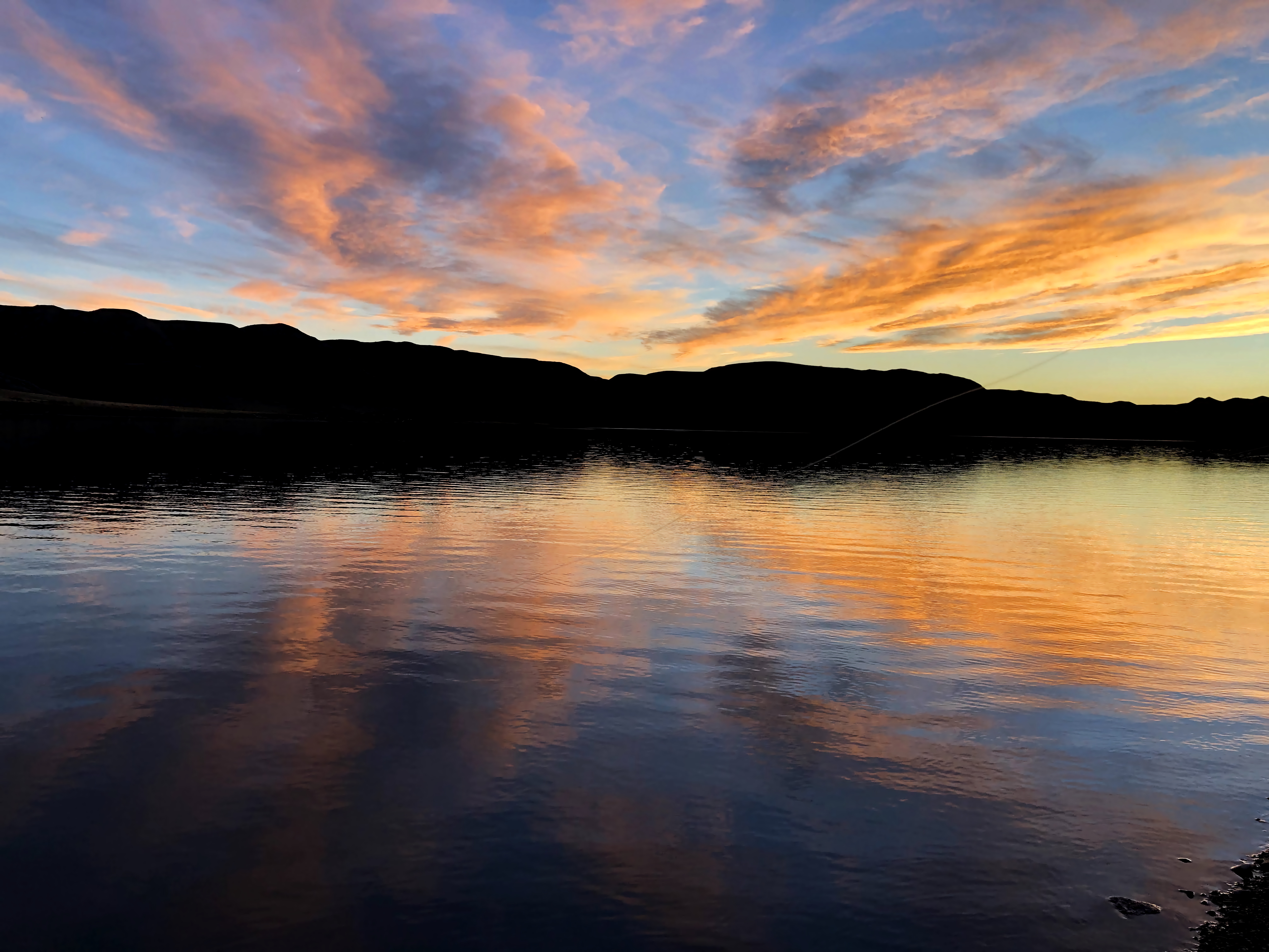 a sunset over a lake. you can see beautiful colors all over the rainbow from red to blue. the clouds are thin, so they enhance the effect, while ripples in the water distort the sky above.