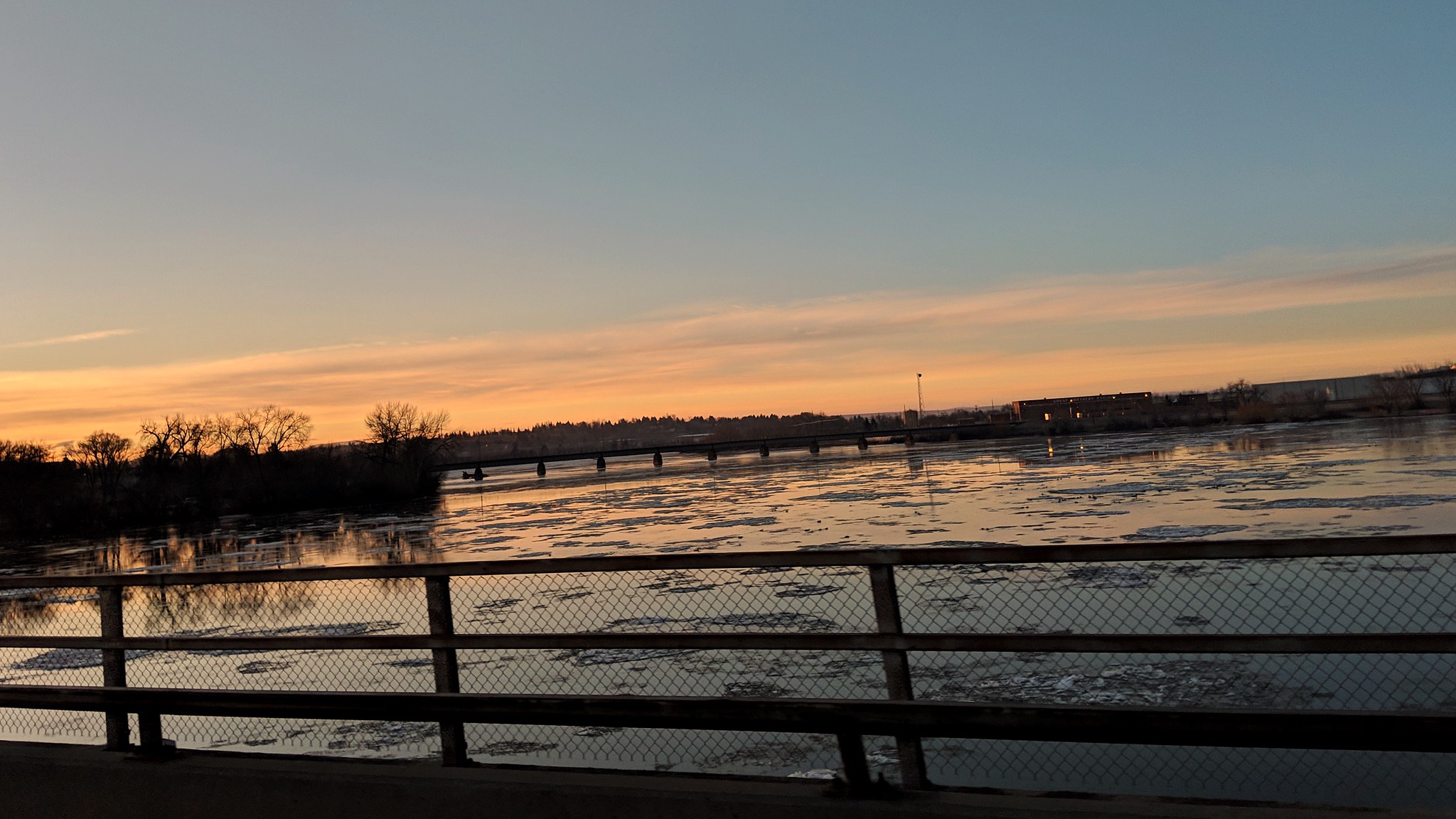 a beautiful sunrise over a rushing recently thawed river. image taken from a bridge, and you can see the guard rail.